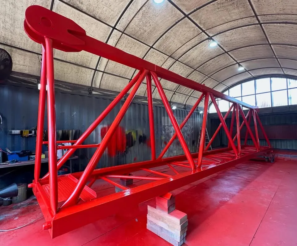 Red lattice crane boom section, sandblasted and painted, on timber blocks